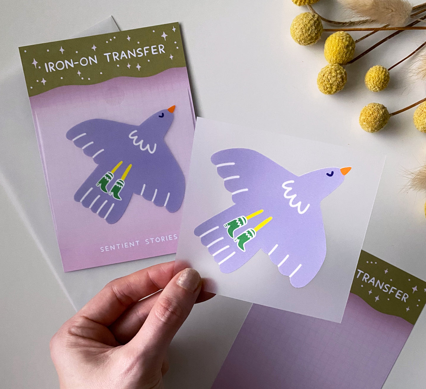 Purple bird design iron-on transfer held by a hand with packaging in the background.