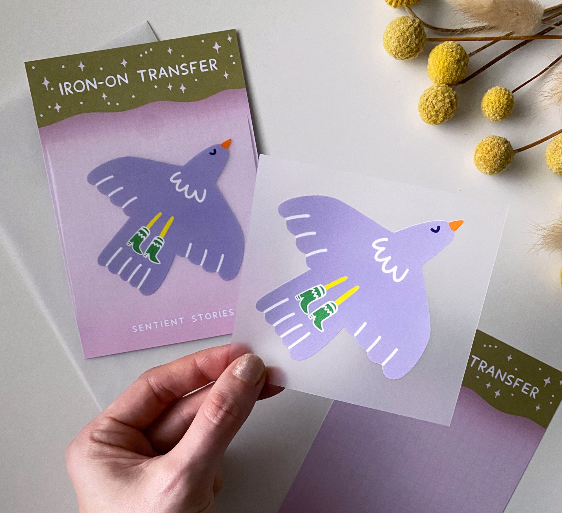 Purple bird design iron-on transfer held by a hand with packaging in the background.