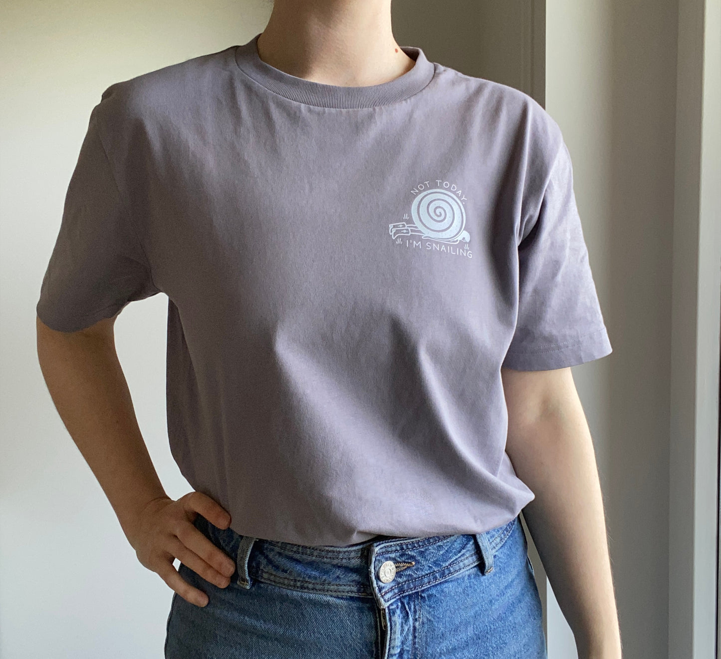 Person wearing an organic cotton gray t-shirt with a snail logo, standing against a neutral background