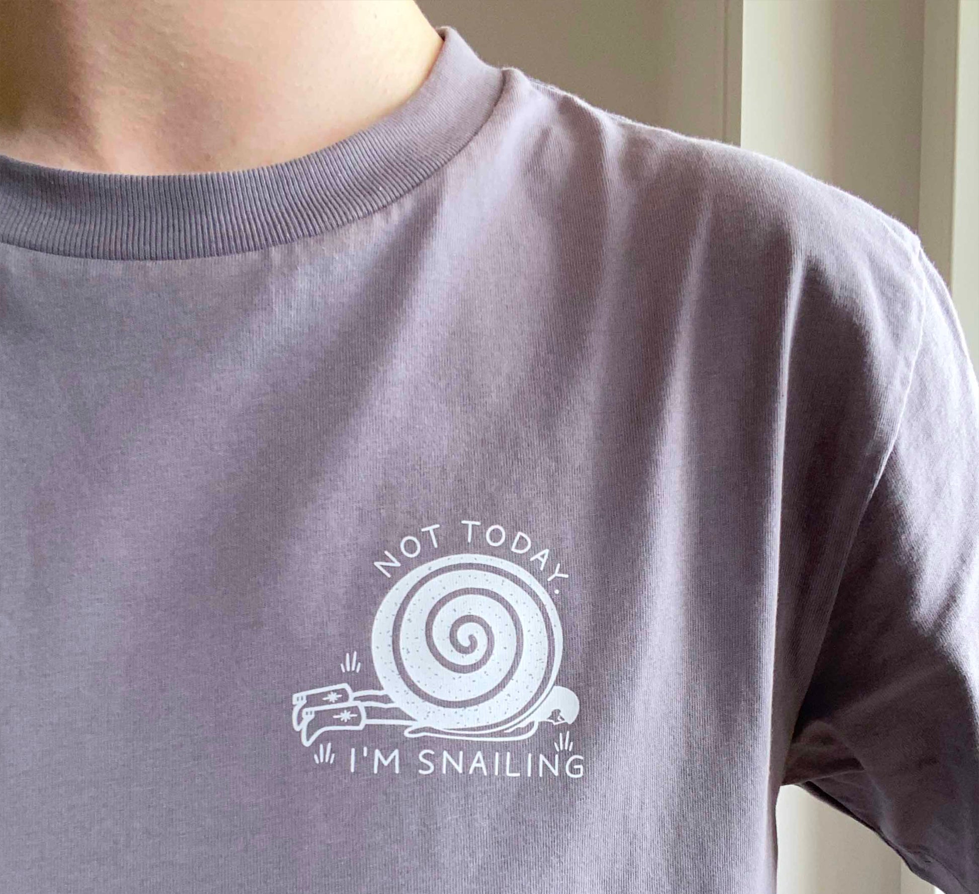 Person wearing an organic cotton gray t-shirt with a snail logo, standing against a neutral background