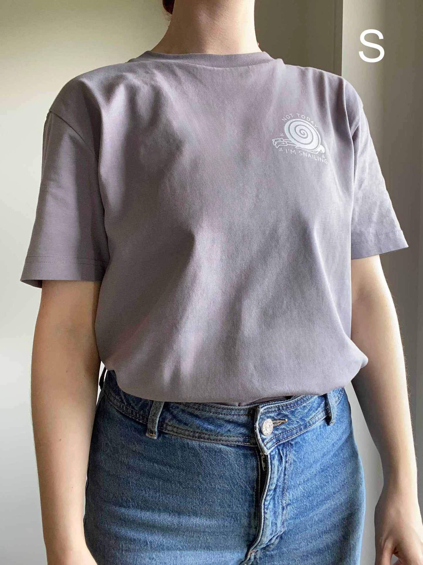 Person wearing an organic cotton gray t-shirt with a snail logo, standing against a neutral background