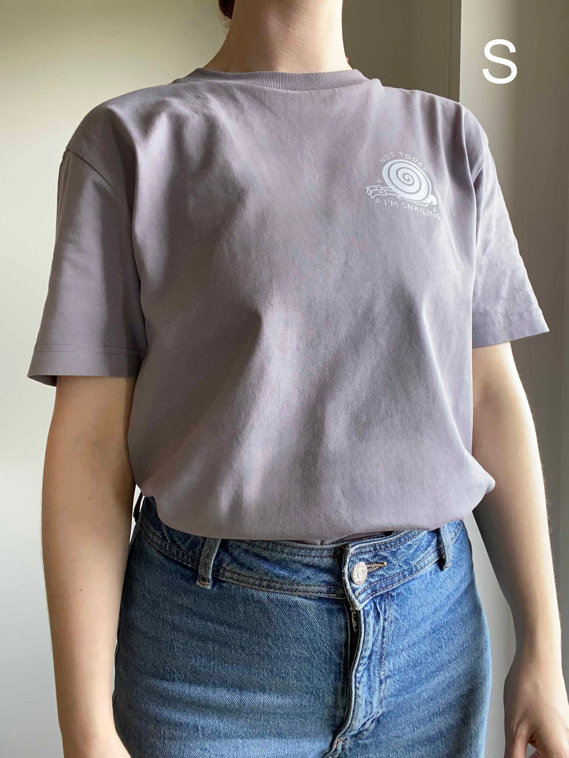 Person wearing an organic cotton gray t-shirt with a snail logo, standing against a neutral background