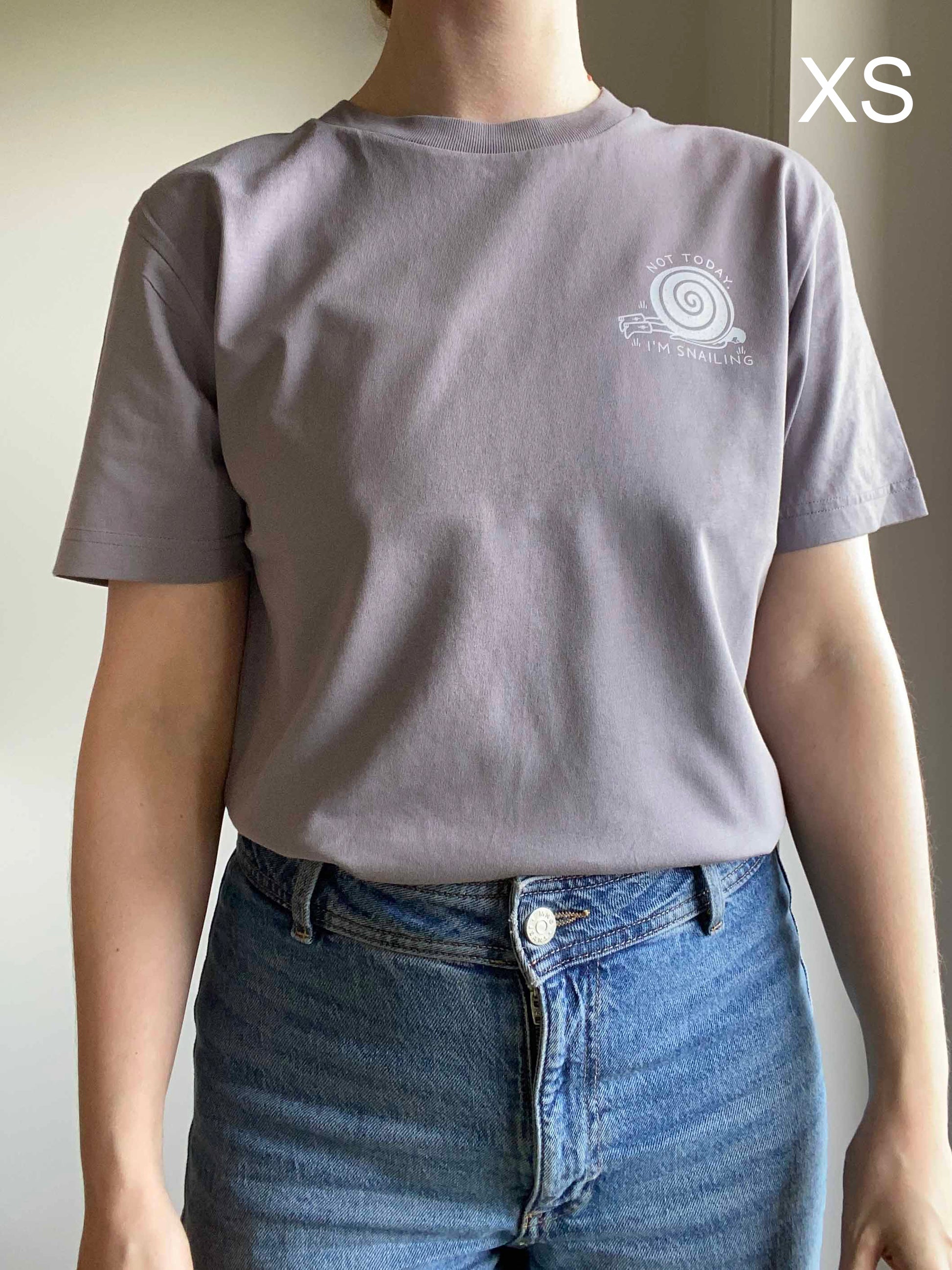 Person wearing an organic cotton gray t-shirt with a snail logo, standing against a neutral background